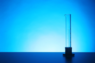 Empty graduated cylinder on table against color background. Chemistry laboratory glassware