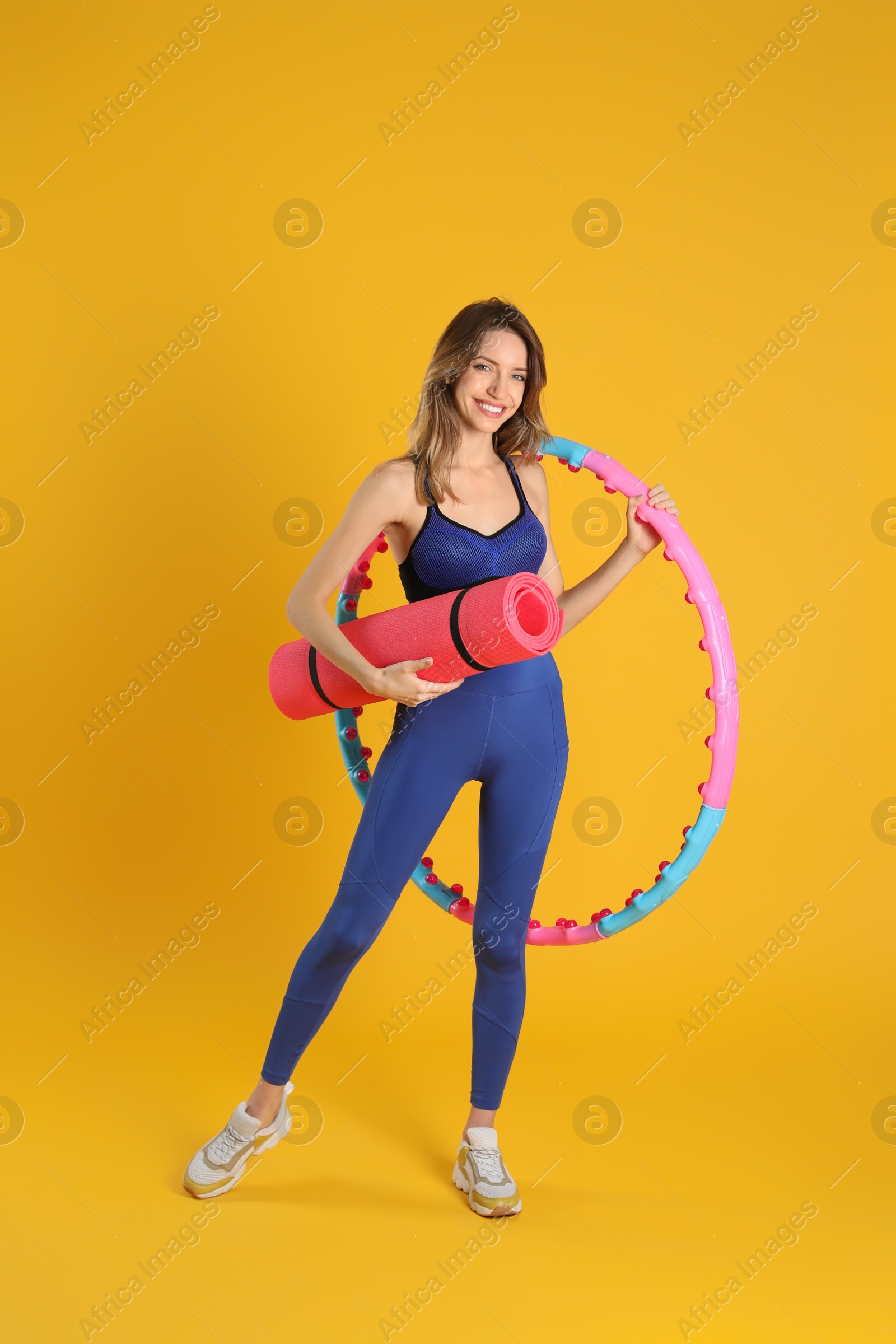 Photo of Beautiful  woman with yoga mat and hula hoop on yellow background