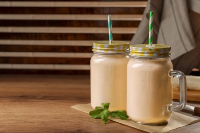 Photo of Tasty banana smoothie and mint on wooden table. Space for text