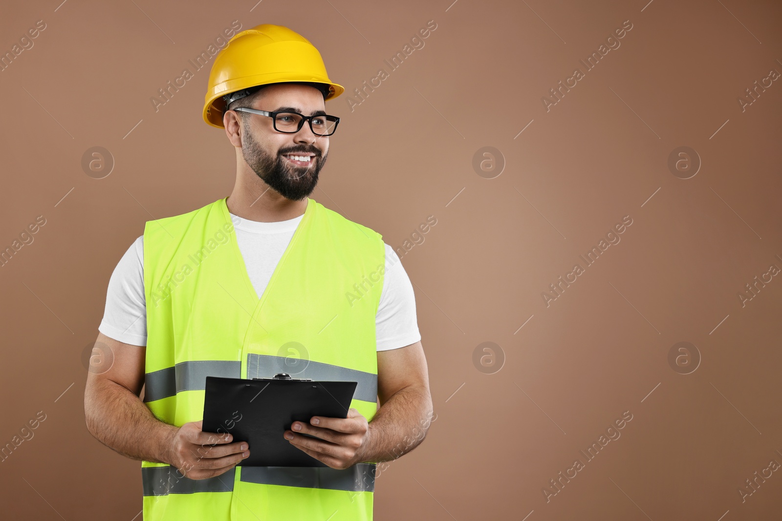 Photo of Engineer in hard hat holding clipboard on brown background