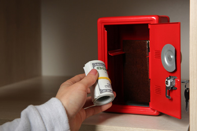 Photo of Woman putting money into red steel safe, closeup