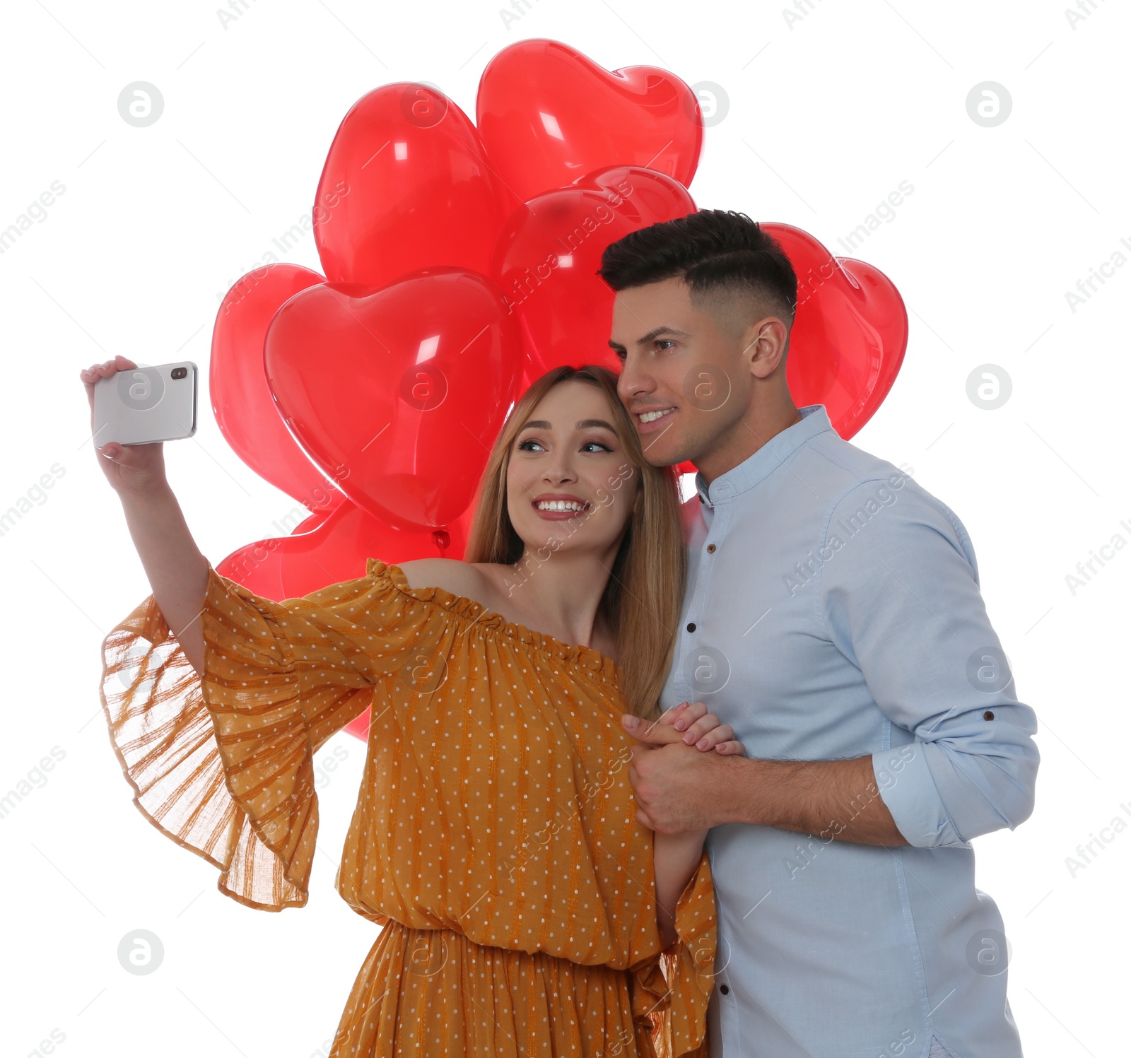 Photo of Lovely couple with heart shaped balloons taking selfie on white background. Valentine's day celebration