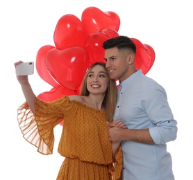 Photo of Lovely couple with heart shaped balloons taking selfie on white background. Valentine's day celebration