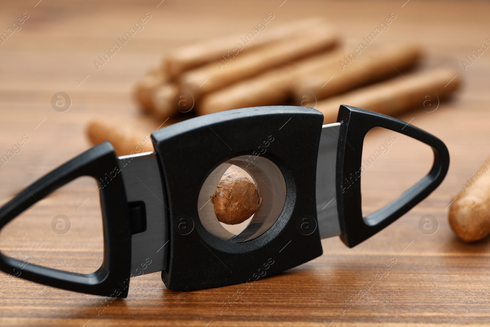 Photo of Cigars and guillotine cutter on wooden table, closeup