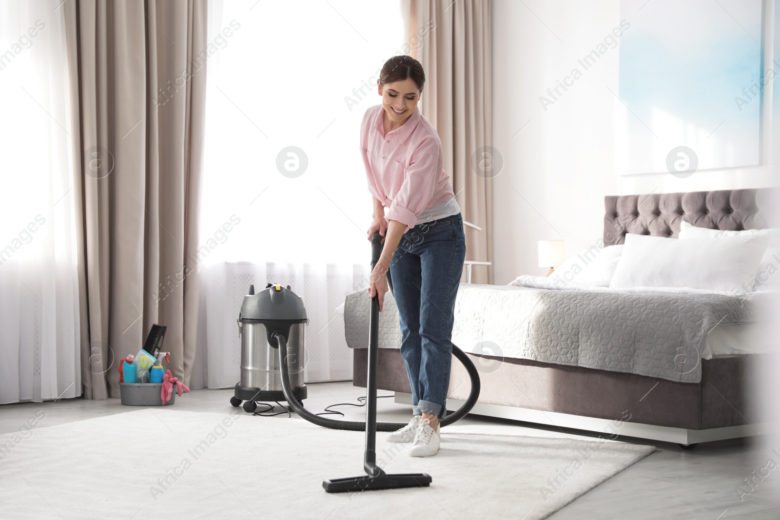 Photo of Woman removing dirt from carpet with vacuum cleaner at home