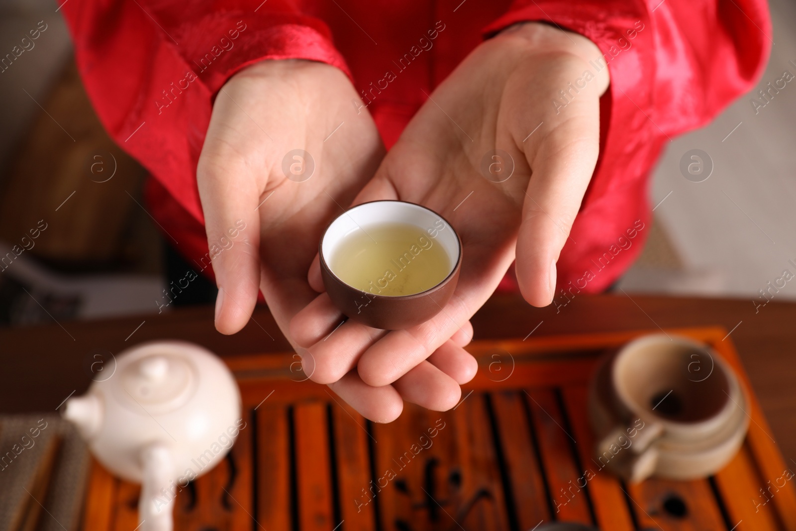 Photo of Master offering cup of freshly brewed tea during traditional ceremony at table, closeup