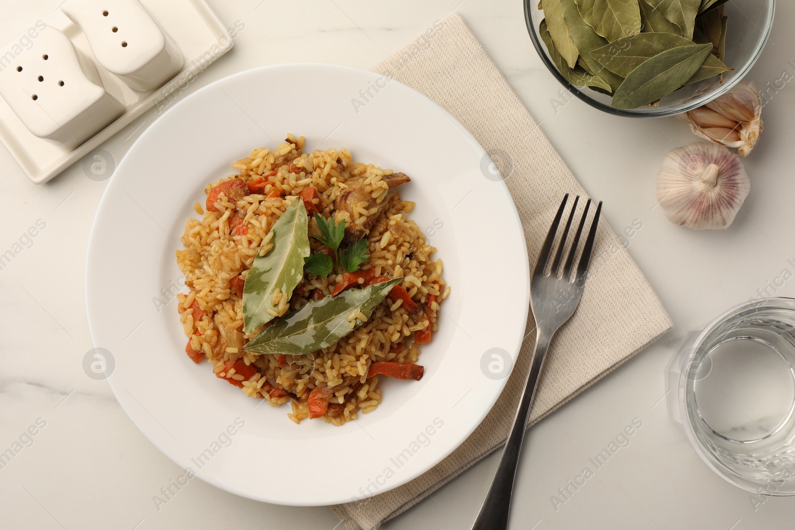 Photo of Delicious pilaf, bay leaves and fork on white table, flat lay