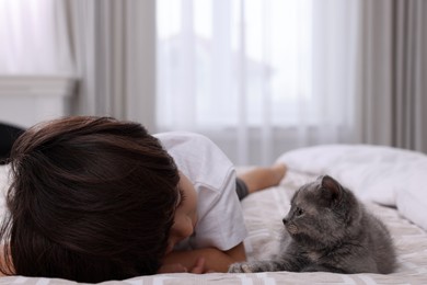 Cute little boy with kitten on bed at home. Childhood pet