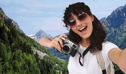 Beautiful woman in sunglasses with camera taking selfie in mountains