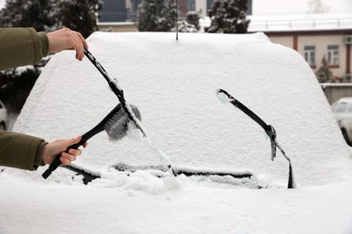 Woman cleaning car wiper blade from snow with brush outdoors, closeup