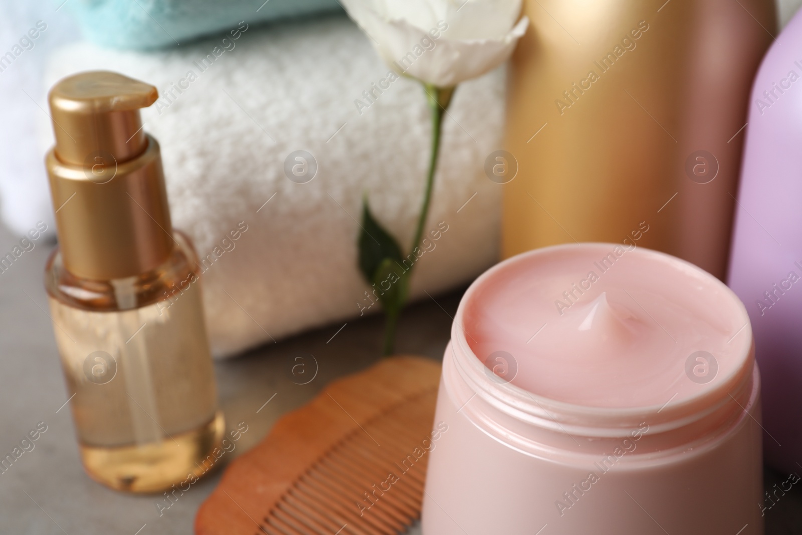 Photo of Different hair products, flower and wooden comb on grey table, closeup