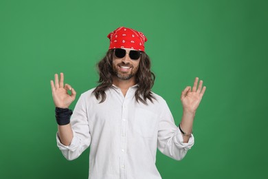 Photo of Stylish hippie man in sunglasses showing OK gesture on green background