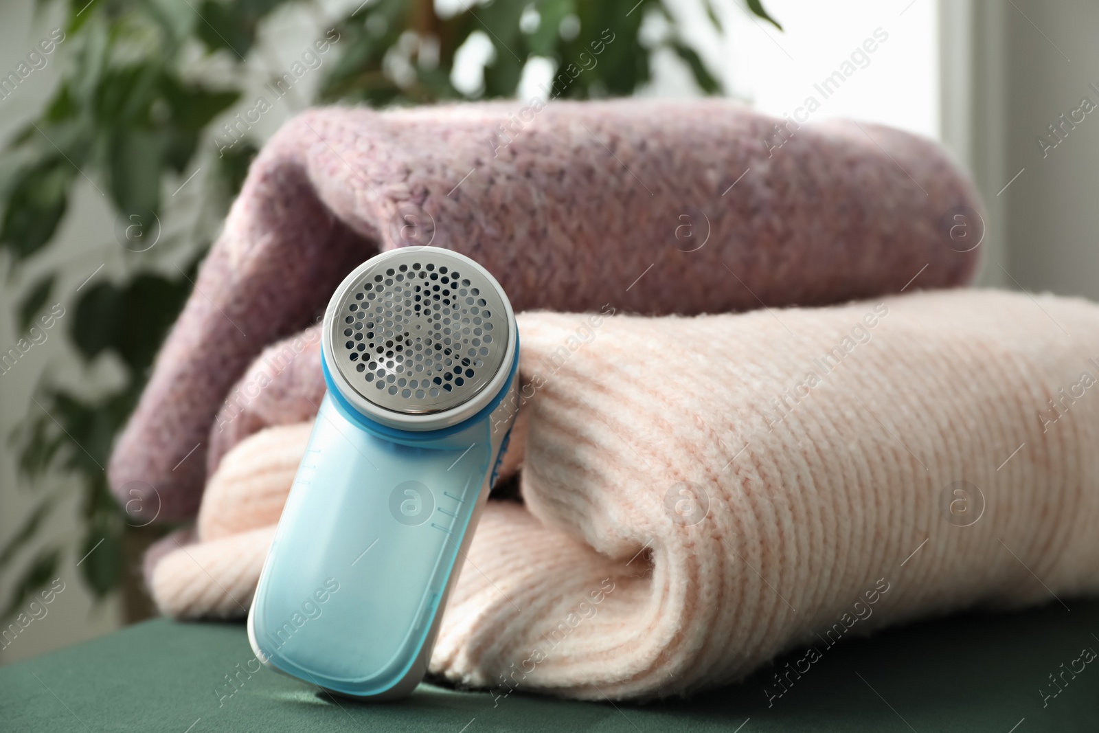 Photo of Modern fabric shaver and woolen sweaters indoors, closeup