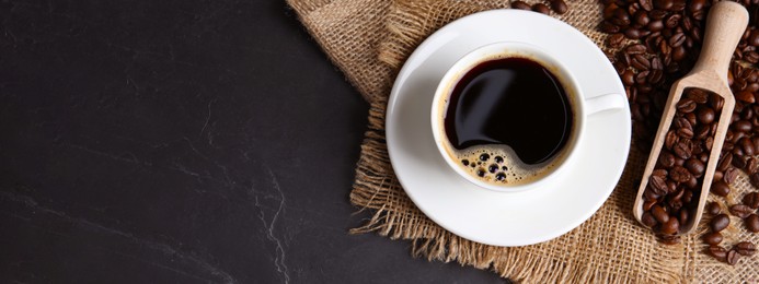 Image of Cup of hot aromatic coffee and scoop with roasted beans on black table, top view with space for text. Banner design