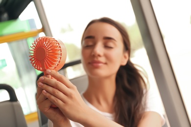 Photo of Woman with portable fan in bus, focus on hands. Summer heat