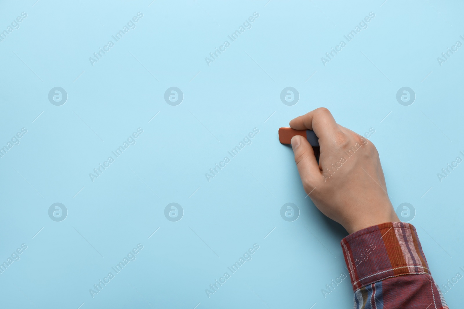 Photo of Man erasing something on light blue background, closeup. Space for text