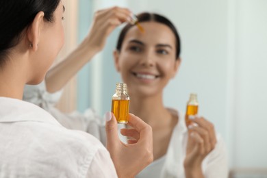 Photo of Young woman with bottle of essential oil near mirror, closeup