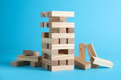 Photo of Jenga tower made of wooden blocks on light blue background
