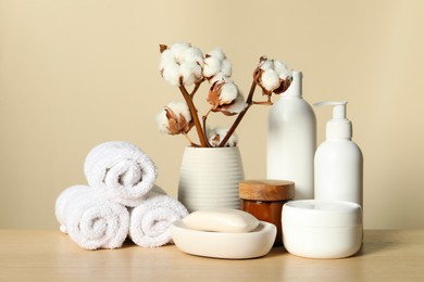 Different bath accessories and cotton flower on wooden table against beige background