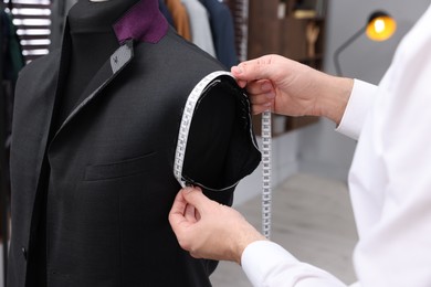 Photo of Tailor working with unfinished suit jacket in atelier, closeup