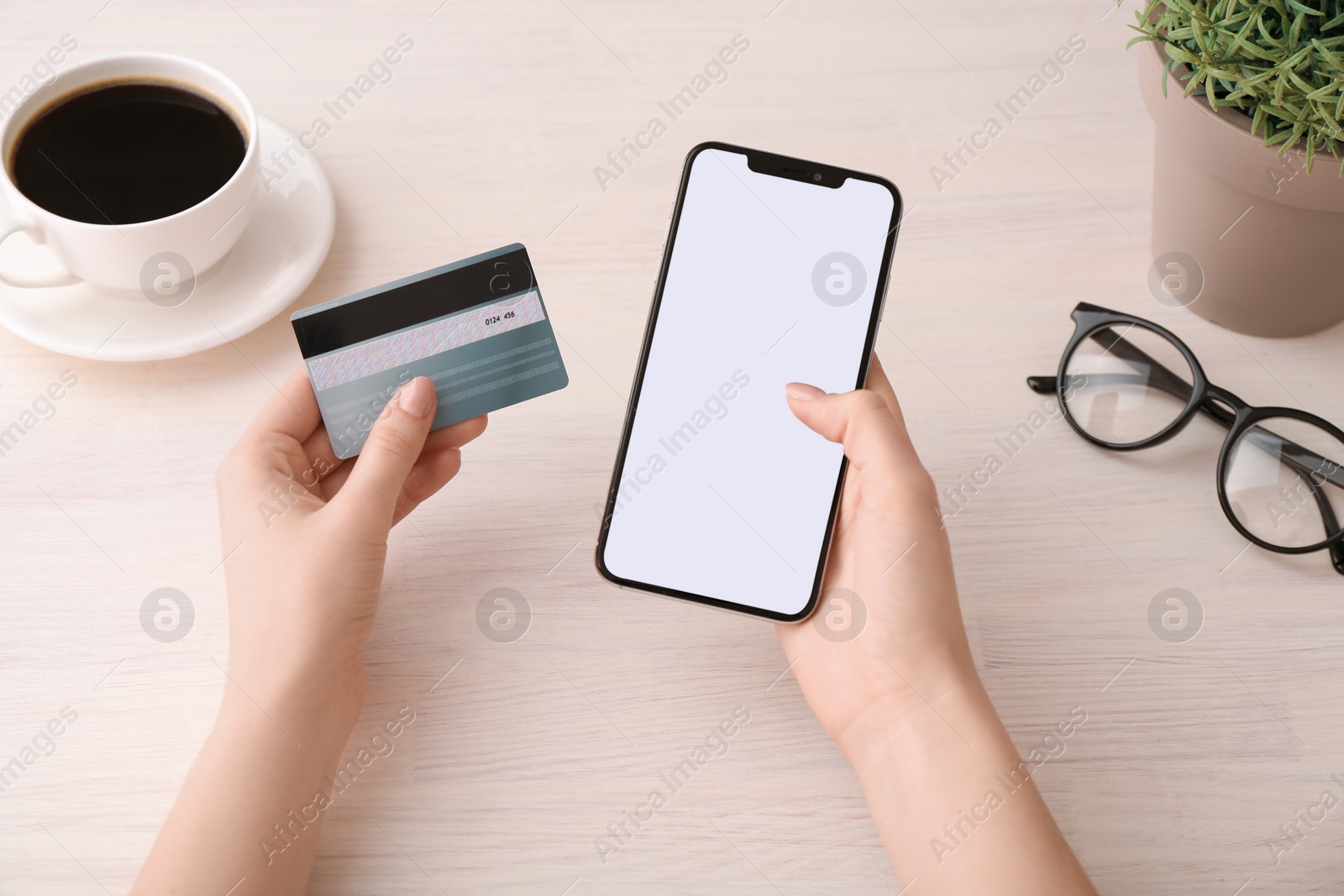 Photo of Online payment. Woman with smartphone, credit card, coffee and glasses at white wooden table, top view