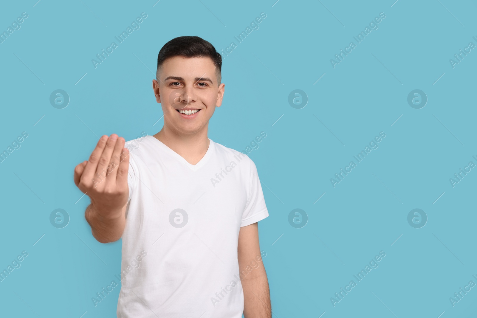 Photo of Handsome man inviting to come in against light blue background. Space for text