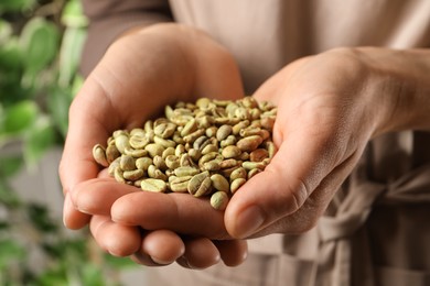 Photo of Woman holding pile of green coffee beans on blurred background, closeup