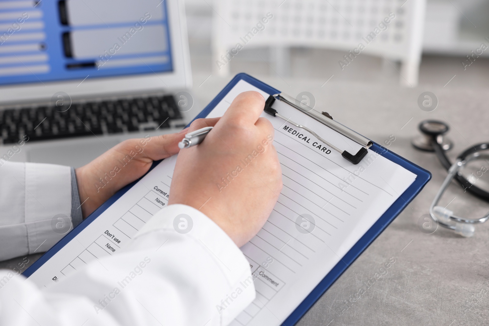 Photo of Doctor filling out patient's medical card at table in clinic, closeup