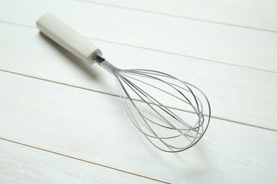 Metal whisk on white wooden table, closeup