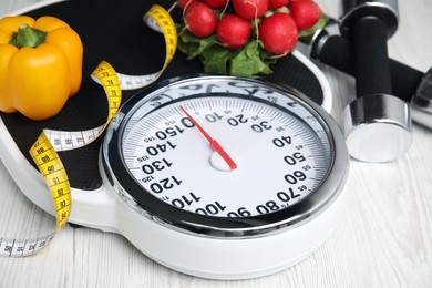 Photo of Scales, healthy food and measuring tape on white wooden table, closeup