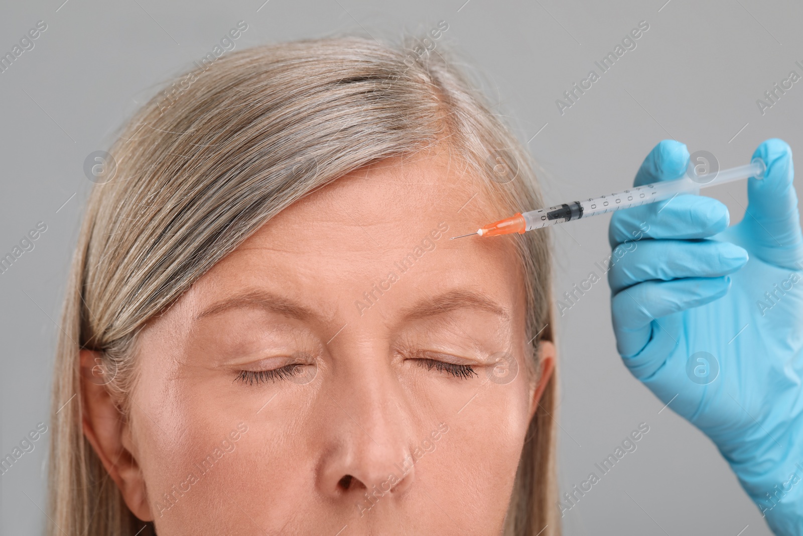 Photo of Doctor giving facial injection to senior woman on light grey background, closeup. Cosmetic surgery