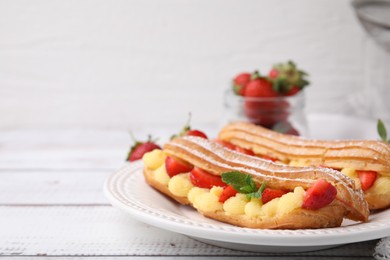 Photo of Delicious eclairs filled with cream, strawberries and mint on white wooden table, closeup