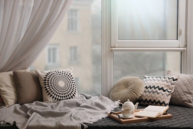 Photo of Comfortable lounge area with blanket and soft pillows near window in room