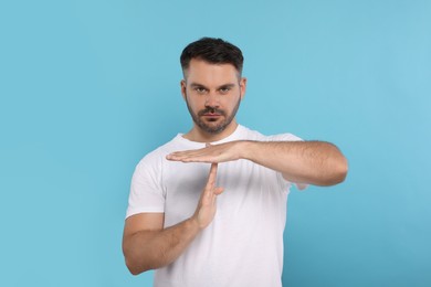 Photo of Handsome man showing time out gesture on light blue background. Stop signal