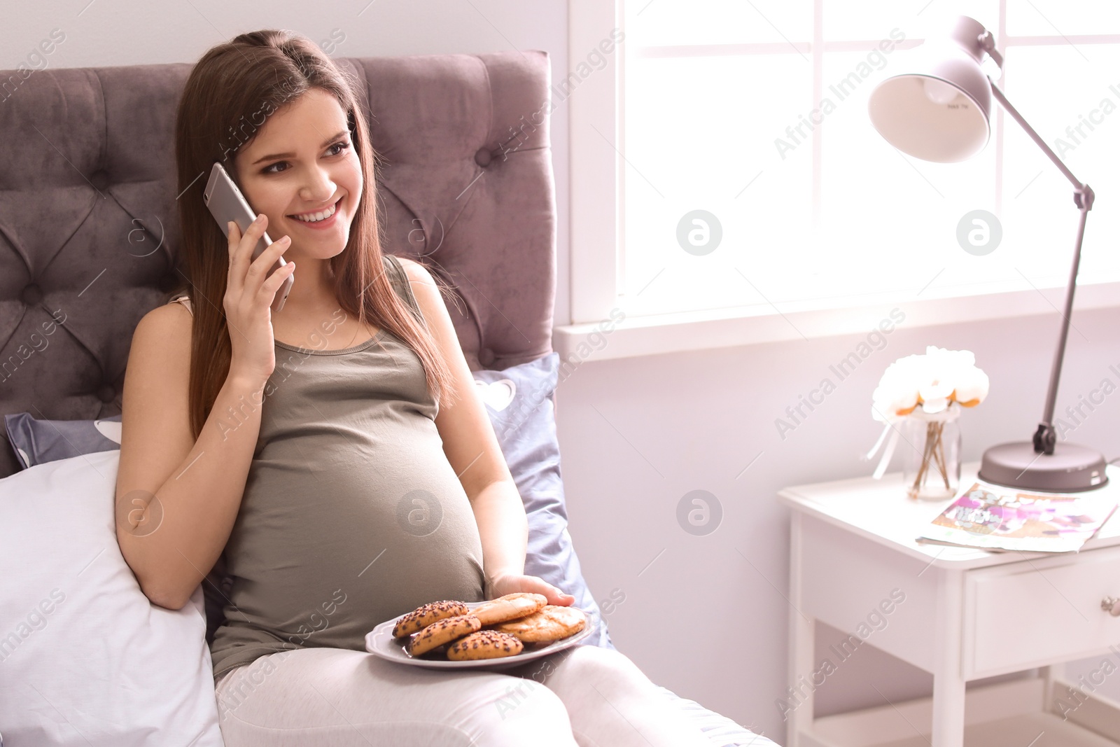 Photo of Young pregnant woman talking by mobile phone on bed