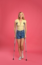 Photo of Young woman with axillary crutches on pink background