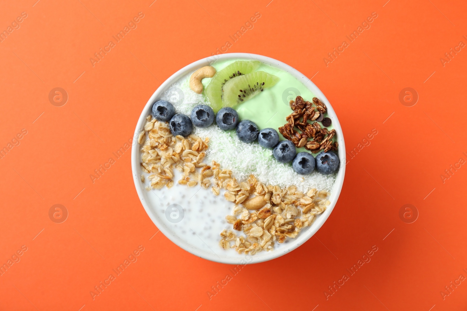 Photo of Tasty smoothie bowl with fresh kiwi fruit, blueberries and oatmeal on orange background, top view