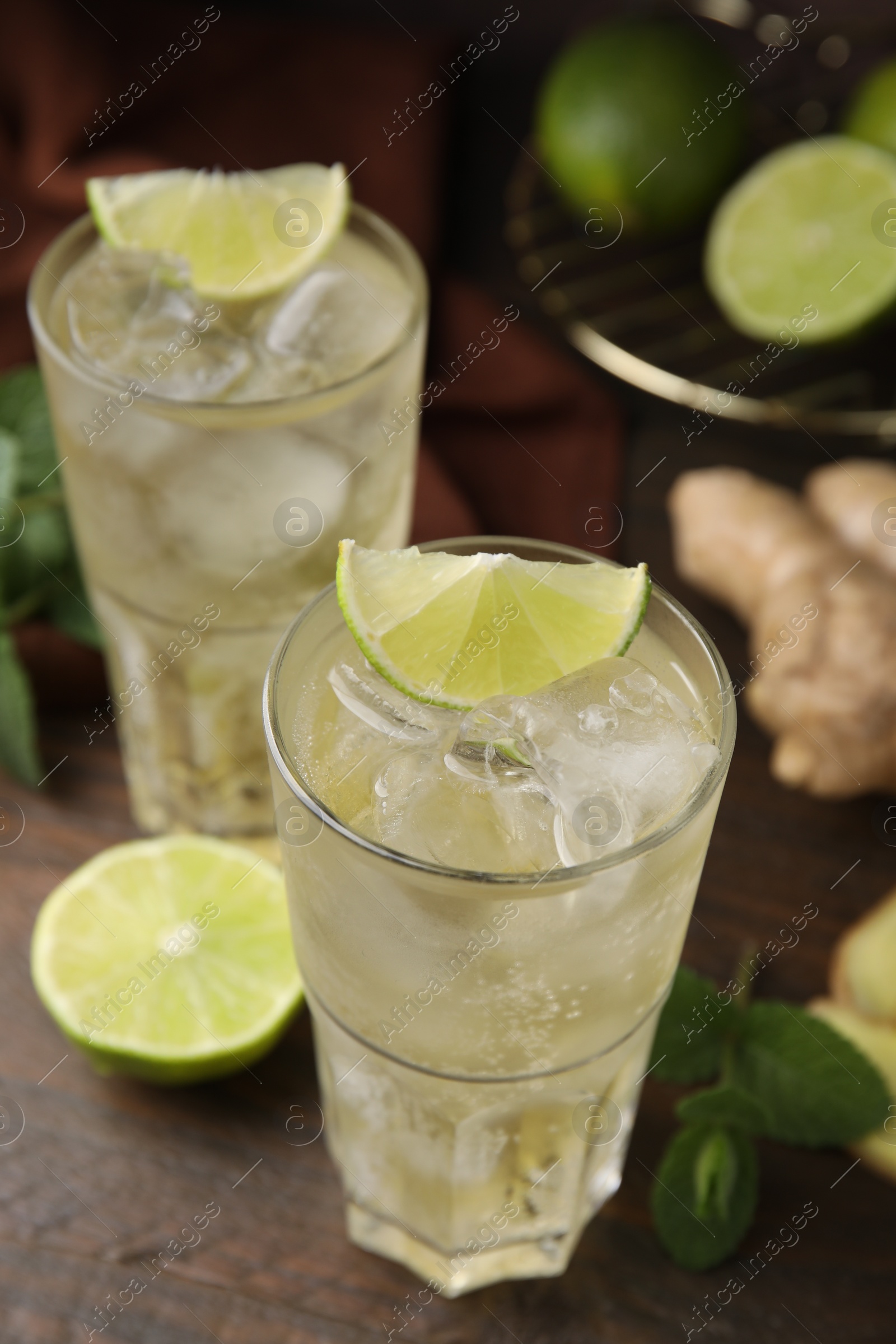 Photo of Glasses of tasty ginger ale with ice cubes and ingredients on wooden table, closeup