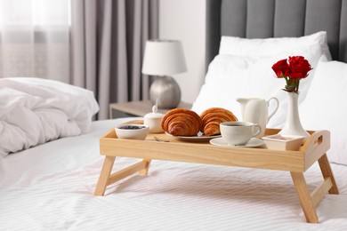 Photo of Wooden tray with tasty breakfast on bed at home