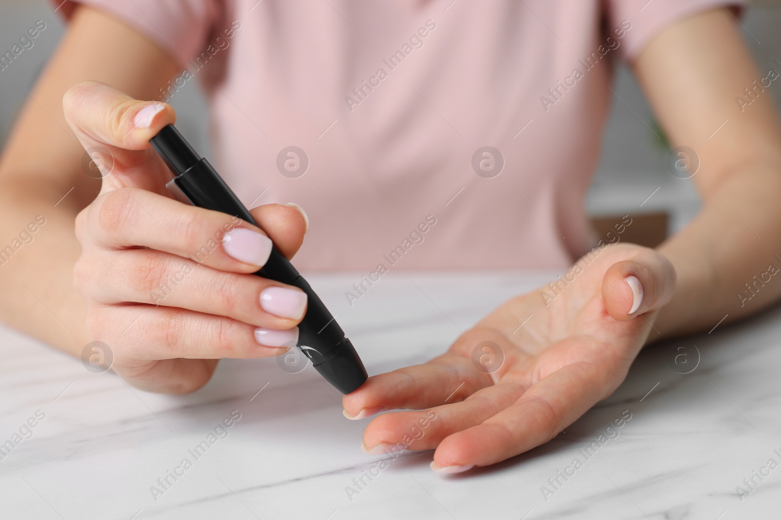 Photo of Diabetes. Woman using lancet pen at white marble table, closeup