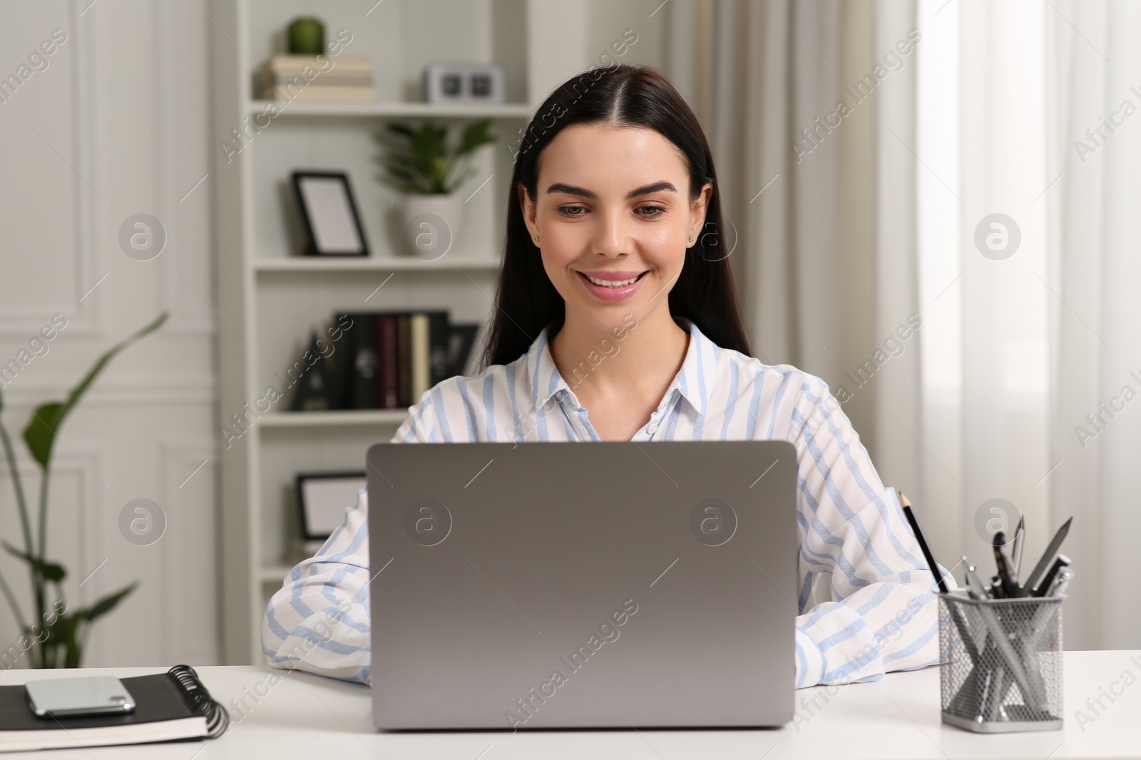 Photo of Happy woman working with laptop at white desk in room