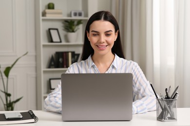 Happy woman working with laptop at white desk in room