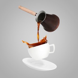 Image of Pouring freshly brewed aromatic coffee from turkish pot into cup. Objects in air on light grey background