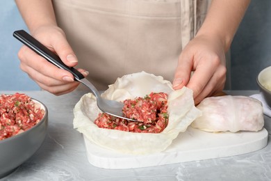 Photo of Woman preparing stuffed cabbage rolls at light grey table, closeup