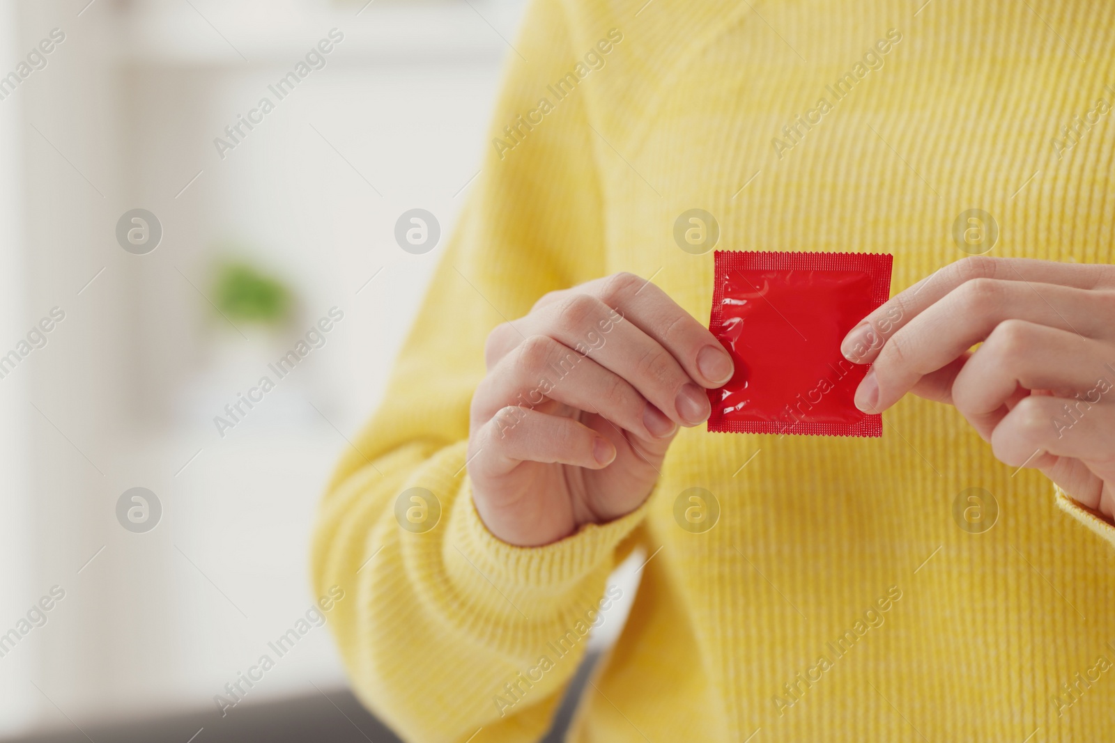 Photo of Woman holding condom indoors, closeup. Safe sex