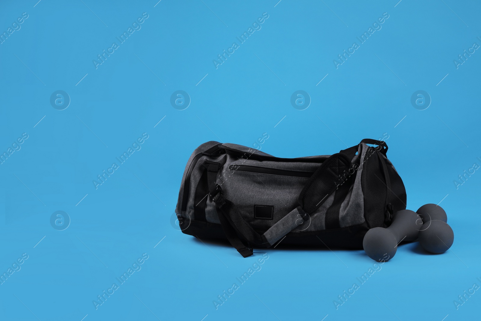 Photo of Grey sports bag and dumbbells on light blue background, space for text