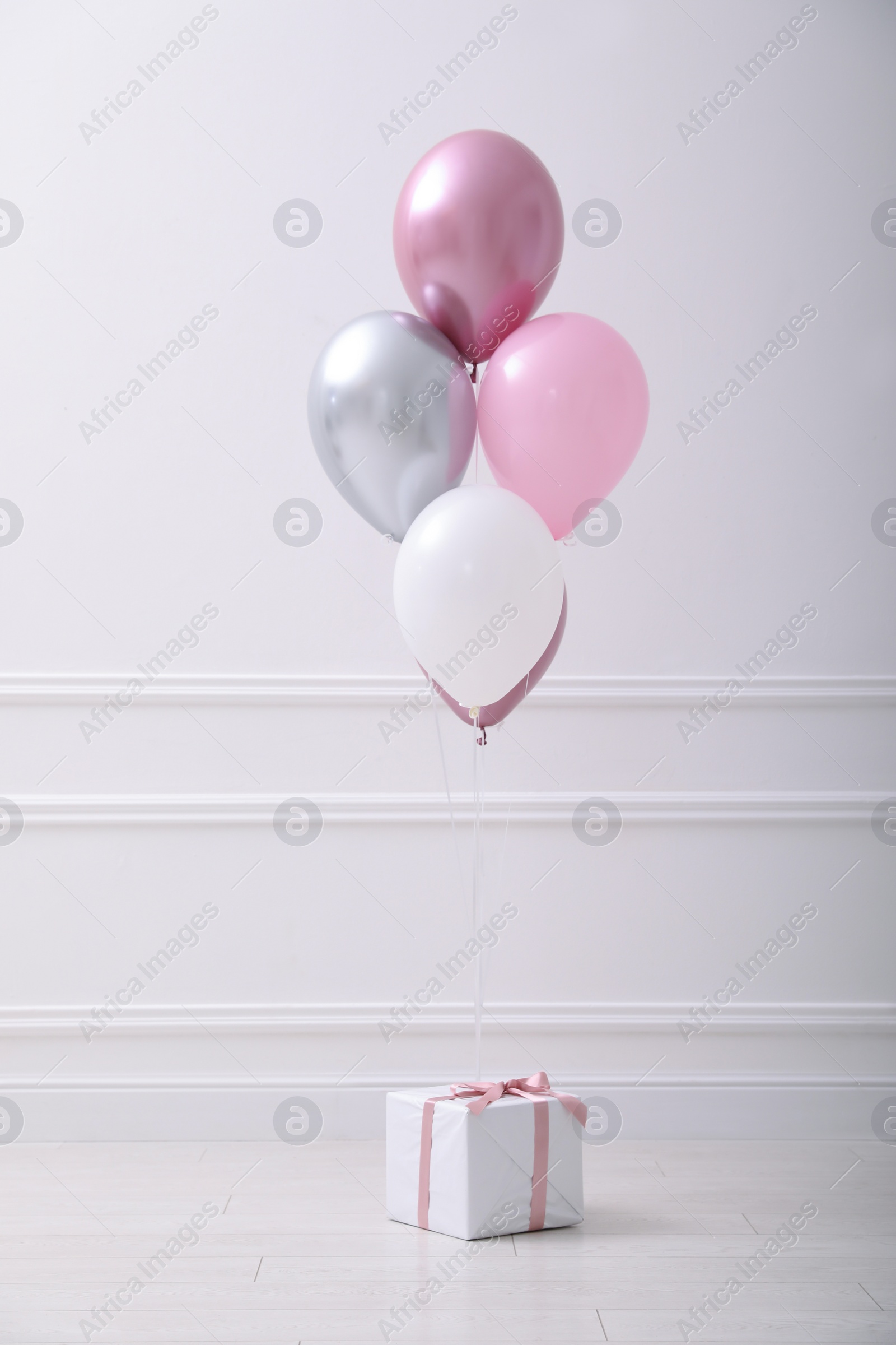 Photo of One gift box and balloons near white wall in room