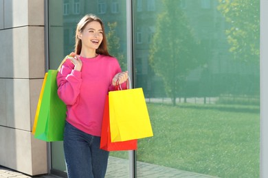 Photo of Beautiful young woman with shopping bags near building outdoors