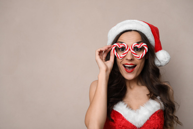 Emotional woman in Christmas costume with party glasses on beige background, space for text