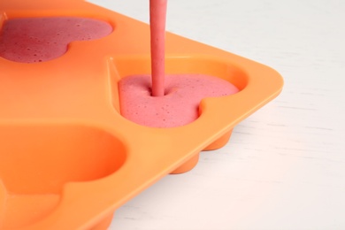 Photo of Pouring smoothie into ice cube tray on table, closeup